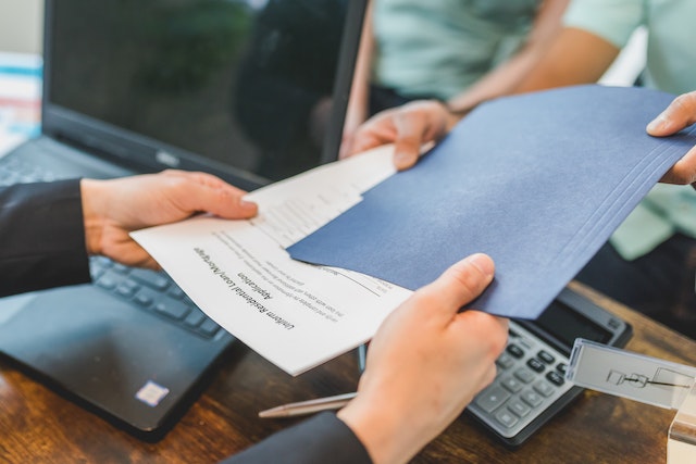 Hands exchanging documents across a desk 